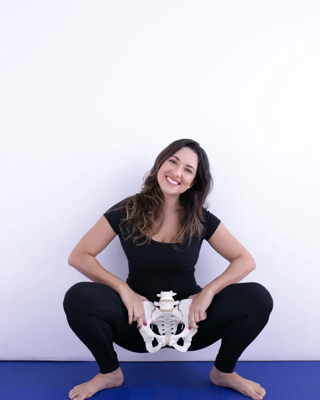 Priscilla em agachamento profundo segurando uma pelve anatômica