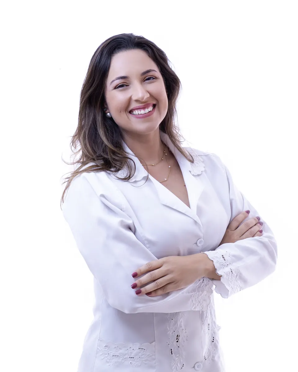Priscilla Valadares, fisioterapeuta obstétrica, sorrindo de jaleco branco e braços cruzados